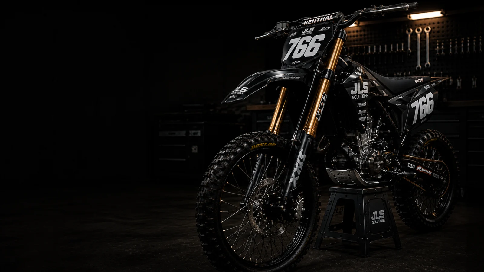 Black factory-style motocross bike number 766 with gold forks in a dark workshop