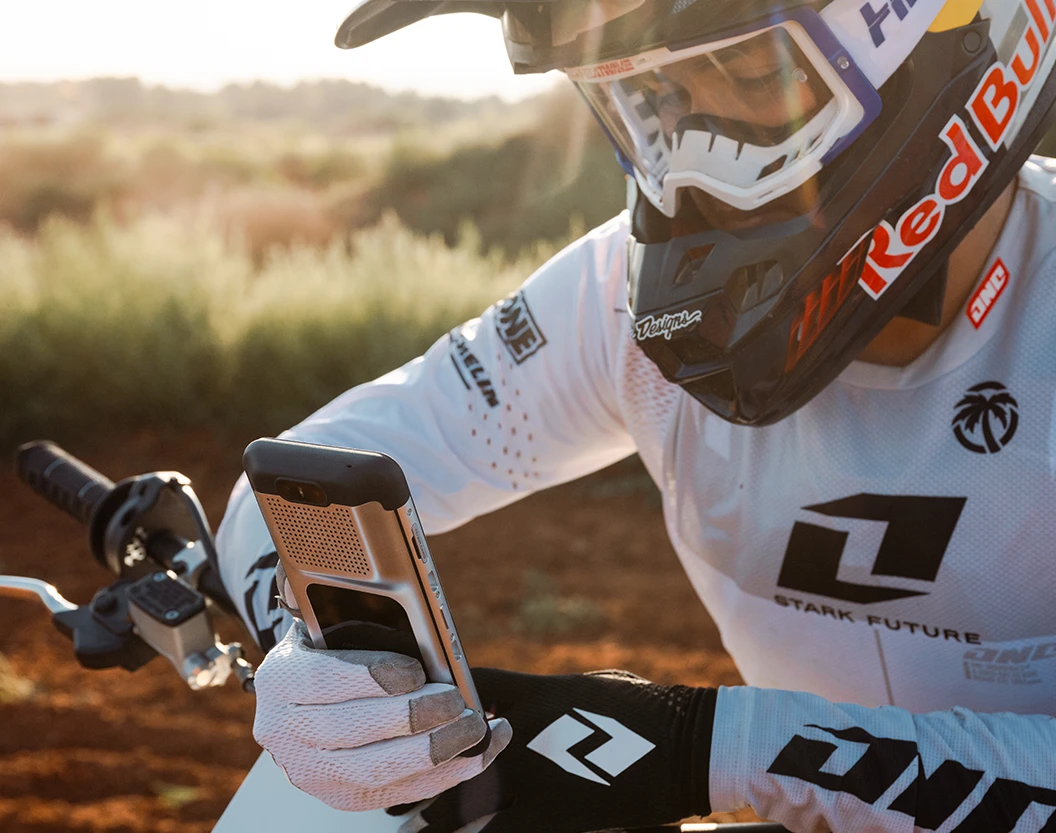 Rider in white Stark Future kit lifting the Varg's removable display unit off its handlebar mount