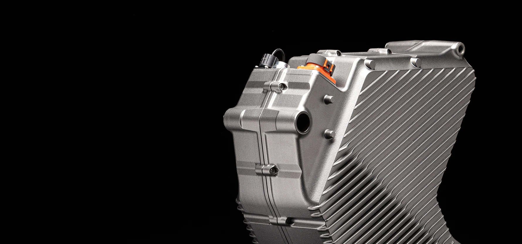 Close view of the Stark Varg's finned aluminium drivetrain housing against black, with an orange high-voltage connector on top