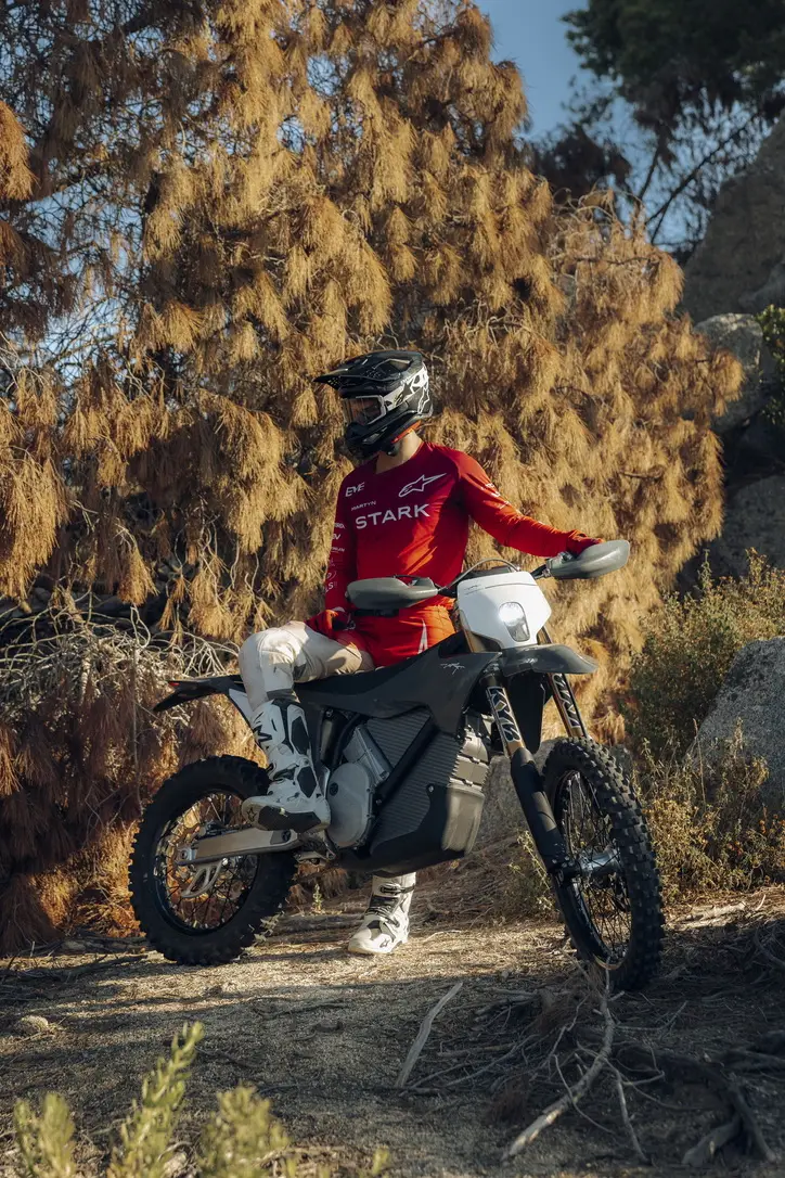 Rider in Stark team kit sitting on a Stark Varg on a dry hillside trail in low afternoon light